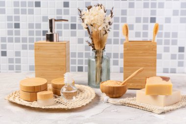 Gri fayans duvarına karşı masasında çiçekler olan banyo malzemeleri.