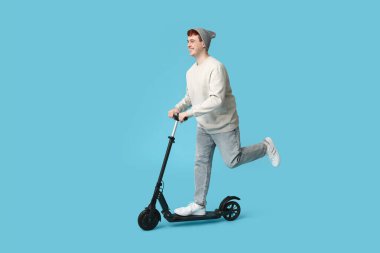 Genç adam mavi arka planda modern elektrikli scooter kullanıyor.
