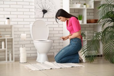 Hamilelik testi olan hasta genç bir kadın tuvalette klozetin yanında.
