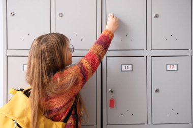 Küçük liseli kız okuldaki dolabını anahtarla kapatıyor.