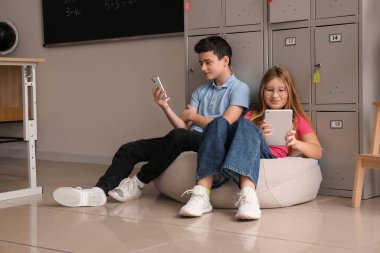 Okuldaki dolabın yanında modern aletler kullanan küçük öğrenciler.