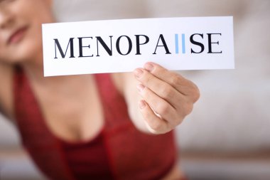 Evde elinde MENOPAUSE sözcüğüyle kağıt tutan sportif olgun kadın, yakın plan.