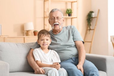 Büyükbaba ve küçük tatlı torunu evdeki kanepede oturuyor.