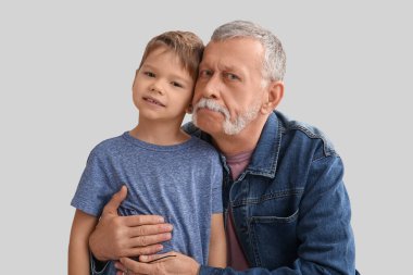 Büyükbaba gri arka planda küçük mutlu torununa sarılıyor.