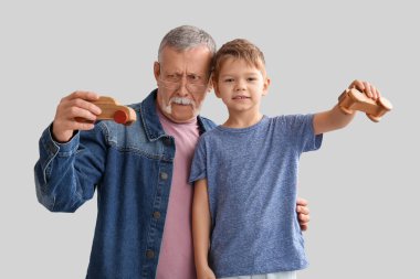 Büyükbaba ve mutlu küçük torunu gri arka planda tahta oyuncaklarla oynuyorlar.