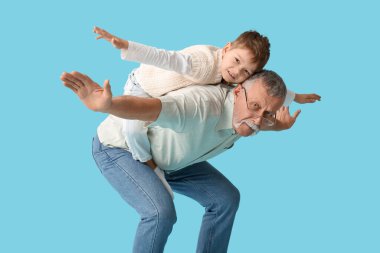 Büyükbaba ve küçük mutlu torunu mavi arka planda birlikte eğleniyorlar.