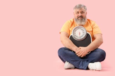 Pembe arka planda oturan kilolu, mutlu, olgun bir adam. Kilo verme konsepti