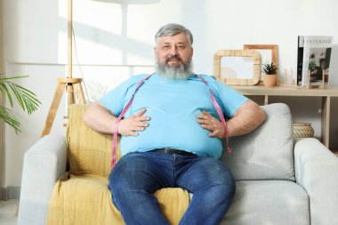 Evdeki kanepede oturan kilolu, mutlu, olgun bir adam. Kilo verme konsepti