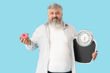 Aşırı kilolu, mutlu, donut ve mavi arkaplanda pulları olan bir adam. Kilo verme konsepti