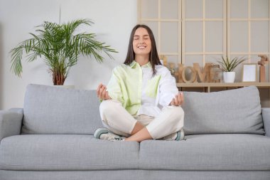 Gri kanepede meditasyon yapan güzel bir kadın.