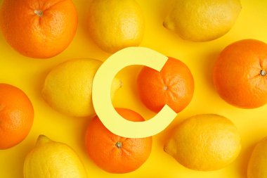 Kağıt C harfli kompozisyon, sarı arka planda taze limon ve portakallar.