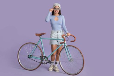 Güneş gözlüklü, leylak arka planda bisikleti olan güzel bir Asyalı kadın.