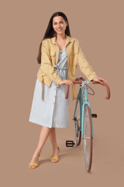 Kahverengi arka planda bisikleti olan güzel genç bir kadın.