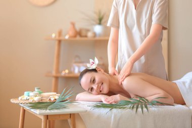 Mutlu genç bir kadın spa salonunda omuzlarına masaj yaptırıyor.