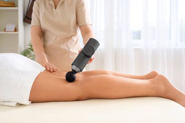 Rehabilitasyon merkezindeki kanepede genç bir kadının bacağına perküsyon masajı yapan kadın terapist.