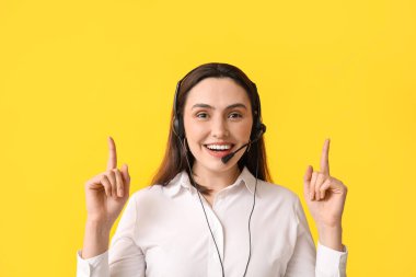 Kulaklıklı kadın teknik destek ajanı sarı arka plandaki bir şeyi işaret ediyor.