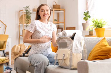 Evde tatil yapmak için havluları sırt çantasına koyan hamile bir kadın.
