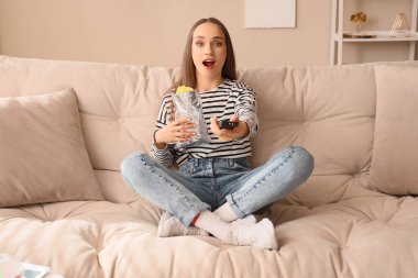 Evde televizyon izleyen patates cipsli genç bir kadın.