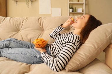 Evdeki kanepede nefis cips yiyen genç bir kadın.