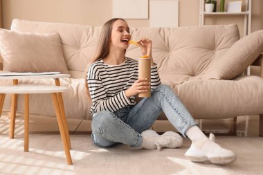 Evde yerde patates cipsi yiyen genç bir kadın.