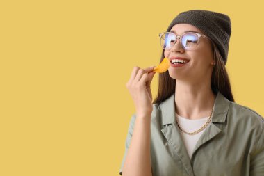 Sarı arka planda patates cipsi yiyen genç kadın, yakın plan.