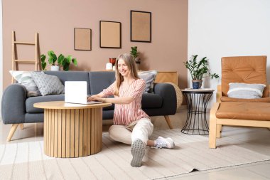 Genç ve güzel bir kadın modern dizüstü bilgisayarını şık oturma odasında kullanıyor.