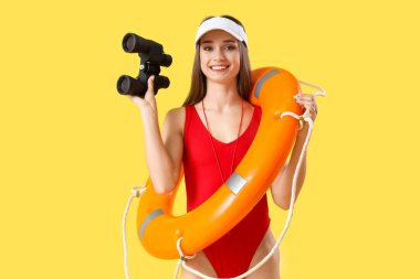 Kurtarma yüzüğüyle şapkalı genç bayan cankurtaran ve sarı arka planda dürbün.