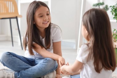 Küçük şirin Asyalı mutlu kız kardeşler evde yerde oturuyor.