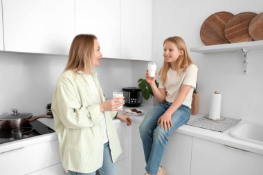 Mutlu kız ve annesi evde oturmuş süt içiyorlar.