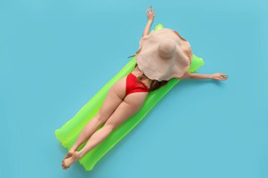 Mayo giymiş güzel bir kadın mavi arka planda şişme yatakta yatıyor.