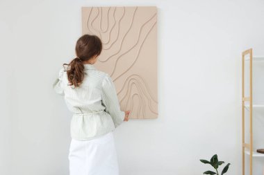 Güzel odadaki beyaz duvara resim asan güzel bir kadın.