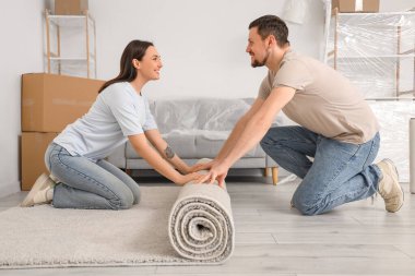 Genç çift taşınma gününde odaya halı seriyor.