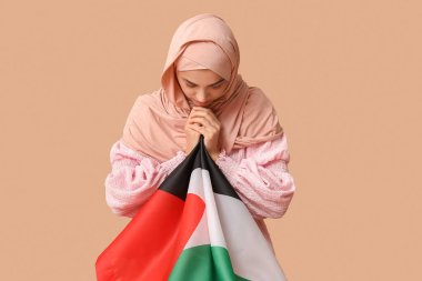 Filistin bayrağıyla bej arka planda dua eden güzel Müslüman kadın. Üzüntü konsepti