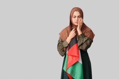 Gri arka planda Filistin bayrağı olan üzgün bir Müslüman kadın. Üzüntü konsepti