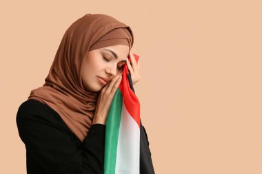 Filistin bayrağı taşıyan genç Müslüman kadın bej arka planda dua ediyor. Üzüntü konsepti