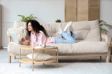Genç Afro-Amerikalı kadın evdeki kanepede dizüstü bilgisayar kullanıyor.