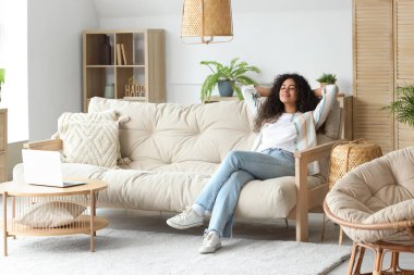 Genç Afro-Amerikalı kadın evdeki kanepede dinleniyor.