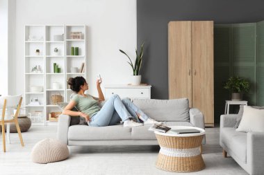 Genç Afro-Amerikalı kadın oturma odasında klimayı açıyor.