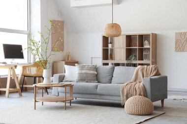 Şık oturma odasının içinde kanepe, sehpa, işyeri ve vazoda çiçek açan ağaç dalları var.