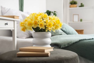 Nergisli vazo ve yatak odasında yeşil pouf üzerine kitaplar, yakın plan.