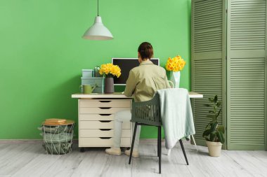 Ofiste masa başında çalışan nergis ve bilgisayarlı genç bir kadın.