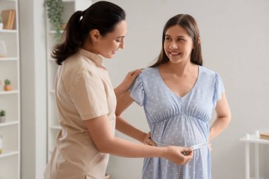 Evde göbek ölçümü yapan hamile bir kadın var.