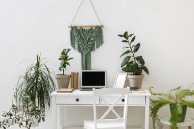 Ofis duvarının yanında dizüstü bilgisayarı ve bitkileri olan modern bir işyeri.