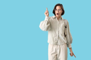 Sırt çantalı bir kız öğrenci mavi arka plandaki bir şeyi işaret ediyor.