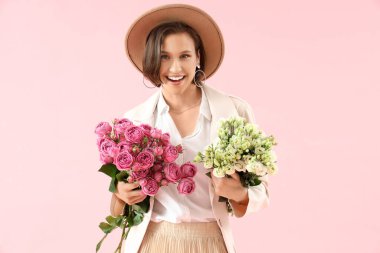 Pembe arka planda çiçekleri olan güzel genç bir kadın.