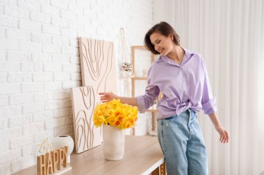 Evdeki vazoda nergisleri olan genç bir kadın.