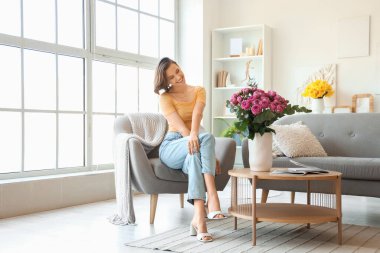 Evdeki koltukta pembe gülleri olan genç bir kadın oturuyor.