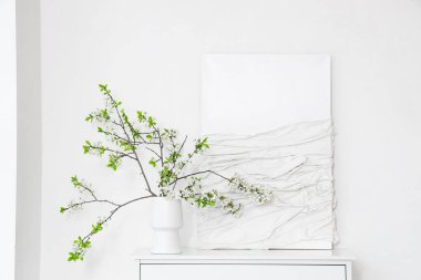 Beyaz odadaki resmin yanındaki masanın üzerinde çiçek açan bir vazo.