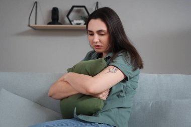 Evdeki kanepede yastıklı depresif genç bir kadın oturuyor.