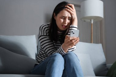 Evdeki koltukta cep telefonu kullanan depresif bir genç kadın.